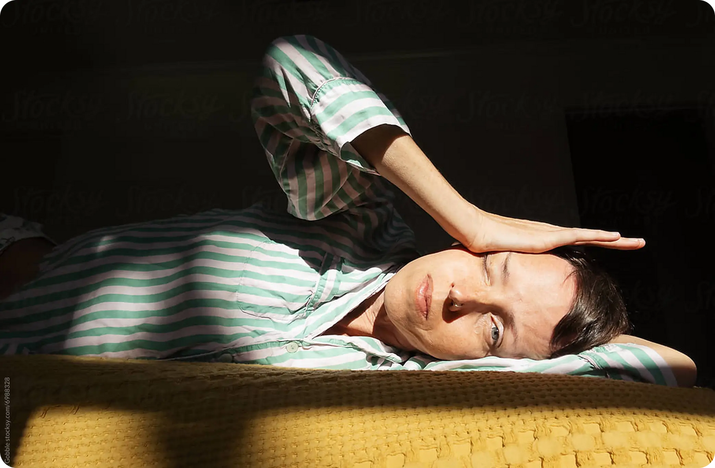 Person holding frozen peas against their head in bed
