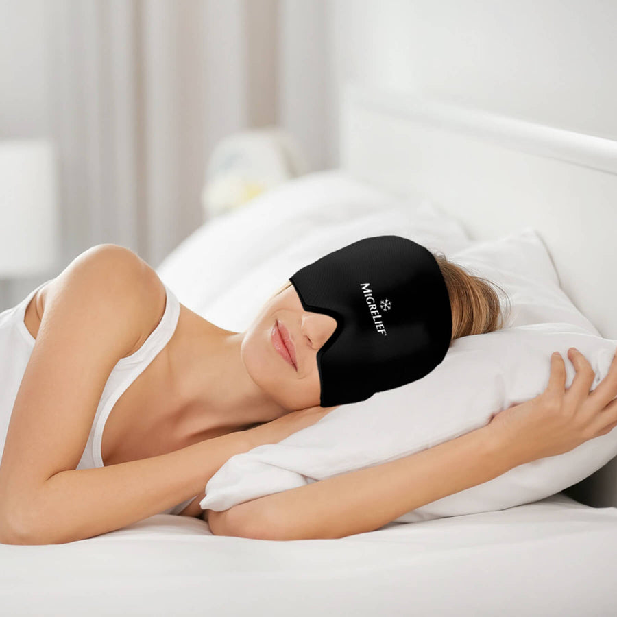 A woman is lying in bed while wearing the MigreLief Cap in black.