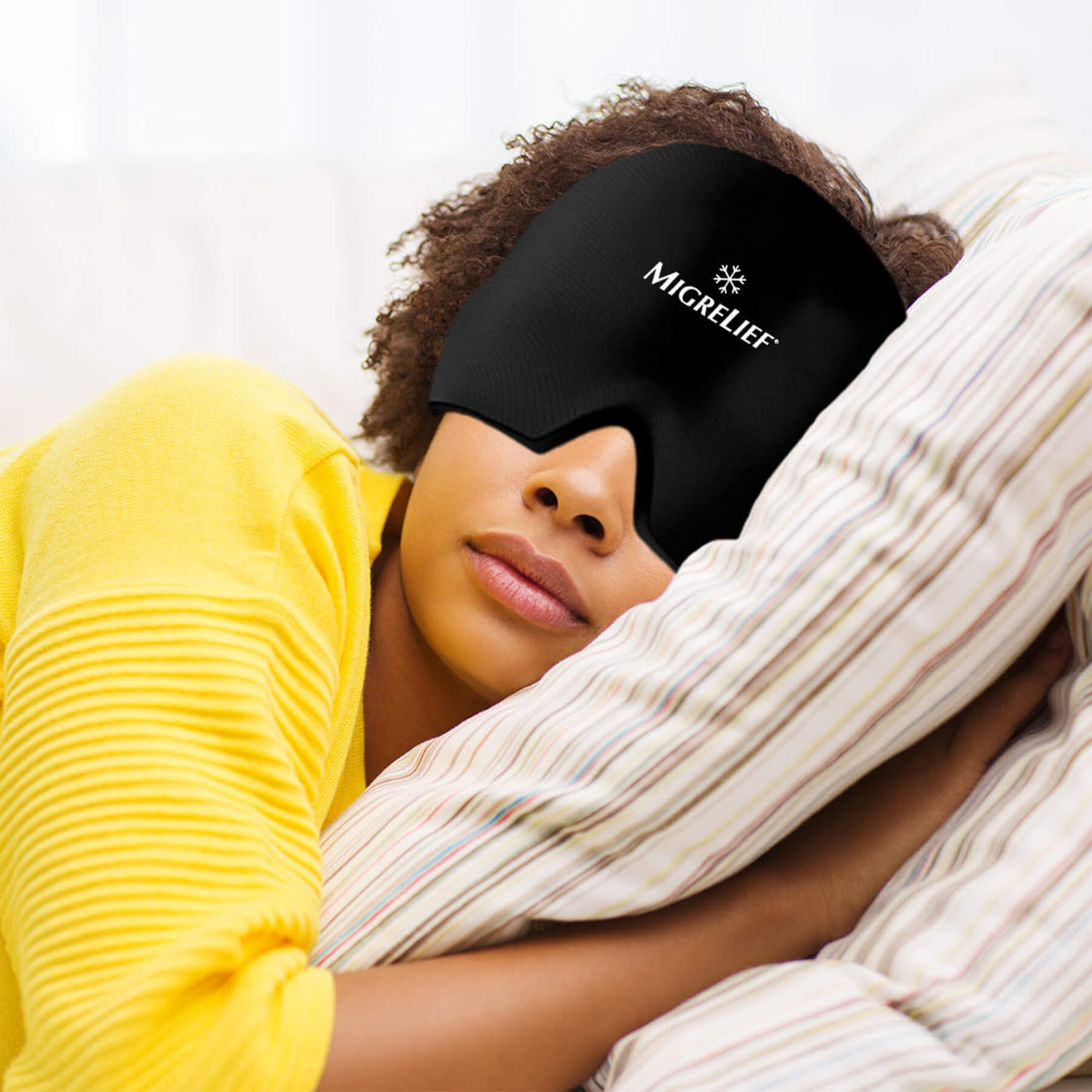A woman rests her head against a pillow while wearing the MigreLief Cap in black.
